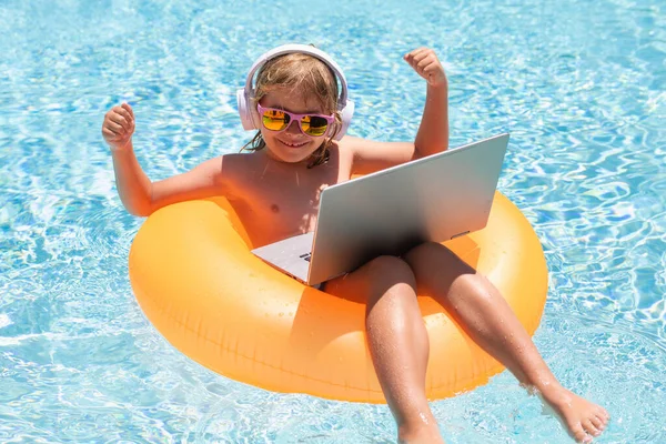 Work outside with laptop in pool. Kid remote working on laptop in pool. Little business man working online on laptop in summer swimming pool water