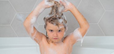 Kid washing hair. Happy funny kid bathed in the bath. Child in shower. Kids face in the bathroom with foam. Portrait of baby bathing in a bath full of foam