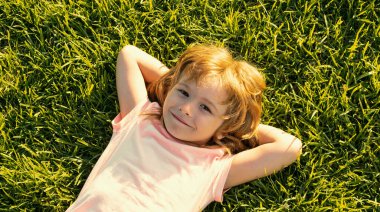 Bahar çocuğu suratlı pankart. Mutlu çocuk çimlerin üzerinde yatıyor. Tatlı çocuk. Tarlada eğleniyor ve hayal kuruyor.