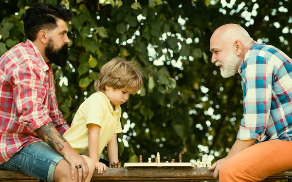 Fathers day. Old man with little boy playing chess. Father and Grandfather with son playing Chess in the park at the day time