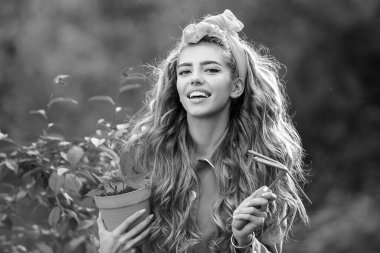 Güzel bir bahçede çalışan ve oynayan güzel bir kadın. Bahar kadını moda konsepti. Gülümseyen büyüleyici kızın portresi elinde saksıyla kameraya bakıyor.