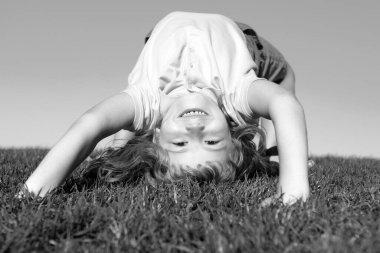 Dışarıdaki çimlerin üzerinde baş aşağı oynayan mutlu bir çocuğun portresi. Gülen çocuk. Etkileyici yüz ifadeleri.