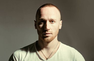 Kızıl sakallı, sakalsız, vahşi bir adam koyu gri arka plan stüdyo fotoğrafında izole edilmiş. Güzel mavi gözlü, kameraya bakan yakışıklı kızıl adam. Alışılmadık erkek görünüşü