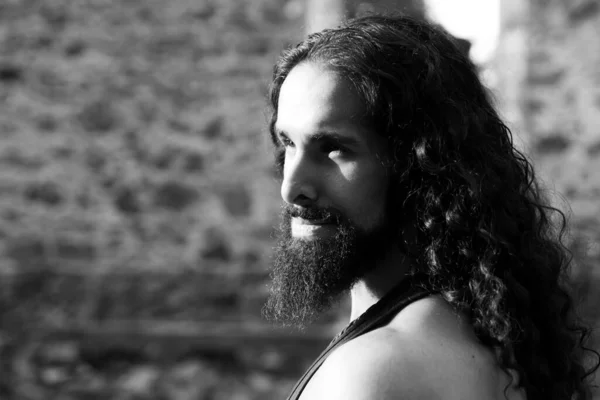 Handsome bearded man with long dark hair. Man style and fashion concept. Close up portrait of handsome man with long dark wavy hair and beard. Confident man with unusual appearance stare straight