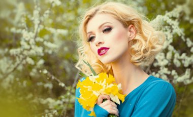 Bahar kadını pankarta karşı. Kıvırcık sarı saçlı, mükemmel tenli ve pembe çiçekli bir yaz bahçesinde güzel makyajlı güzel bir kadının yakın plan portresi.