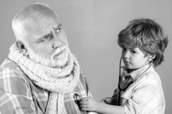 Smiling little boy playing doctor and listening old grandfather with stethoscope. Little doctor. Boy in doctor uniform treat patient