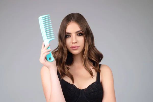 Beautiful model girl with comb brushing hair. Beauty woman with straight hair on studio background. Woman holding hairbrush near face. Healthy hair. Hairstyle and hair care concept. Shiny hairs