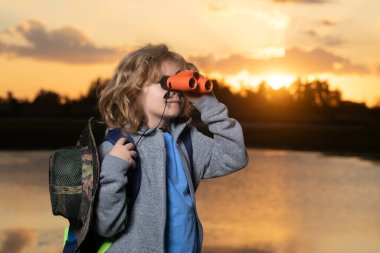Childhood. Young boy looking through binoculars. Explore and adventure. Child boy with backpacks exploring nature and environment. Outdoor leisure activity for children. Summer vacation, tourism