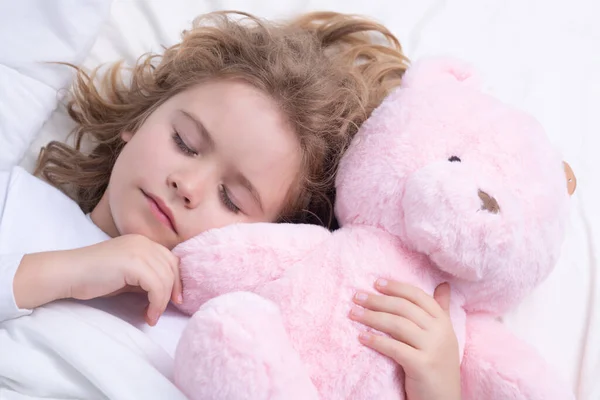 Little boy sleeps. Cute child sleeping with a toy teddy bear on bed at home. Bedtime, kid sleeps. Kid asleep on soft pillow with blanket having healthy sleep