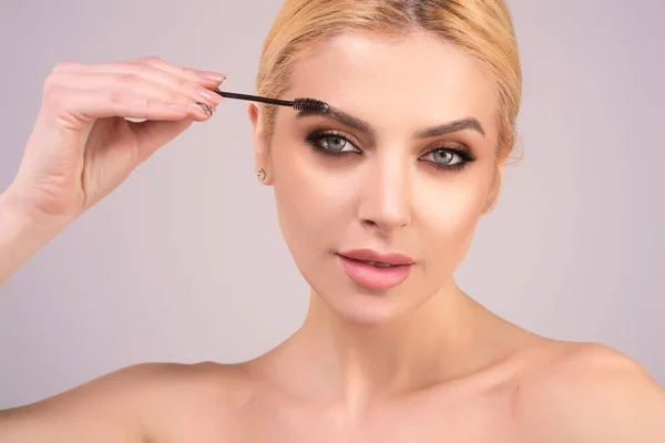 Eyebrow shaping, woman combs eyebrows with a brus. Eyebrow line. Makeup and cosmetology concept. Female model with long eyelashes and thick eyebrows. Perfect shaped brow