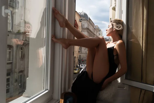 Sensual woman with long slim legs near window in luxury apartment. Seductive woman face. Sensual young woman posing with sexy body. Beautiful sexy model. Beauty face