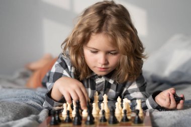 Child playing chess on bed. Clever child thinking about chess. Kids early development