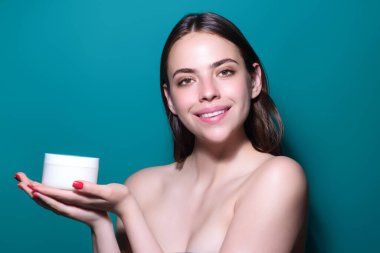 Beautiful model applying cosmetic cream treatment on face. Facial treatment. Beauty portrait of young topless woman with bare shoulders applying face cream
