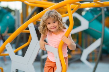 Child climbs up in a park on a playground on a summer day. Childrens playground in a public park. Recreation for children. Kid hanging at outdoor playground