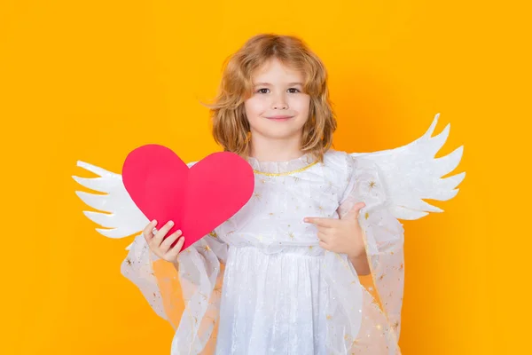 天使指着纸上的红心 点点头 情人节 有天使翅膀的小孩带复制空间的工作室色彩隔离背景下天使儿童的工作室肖像 — 图库照片