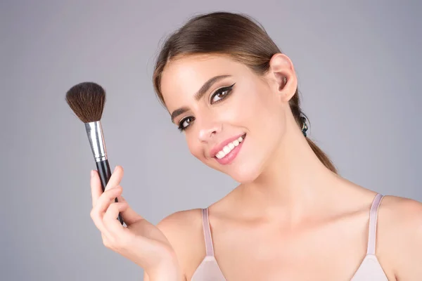 Studio portrait of a woman applying cosmetic tonal foundation on face using makeup brush. Beautiful girl doing contouring apply blush on cheeks isolated on studio background
