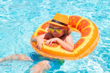 Summer kids Cocktail. Happy little boy with colorful inflatable ring in outdoor swimming pool on summer day. Child swimming in pool play with floating ring