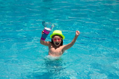 Yüzme havuzunda su sıçratan çocuk. Aktif sağlıklı yaşam tarzı, çocukla yaz tatilinde yüzme sporu aktivitesi. Çocuk kokteyli. Şapkalı ve güneş gözlüklü yaz çocuğu.