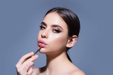 Studio portrait of beautiful woman with red lipstick. Beautiful young woman applying lipstick on her lips, isolated on studio background