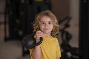 Kid workout kid in gym. Sport activities at leisure with children. Sporty kid boy holding kettlebell