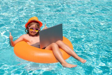 Summer online technology. Child with laptop in swimming pool in summer day