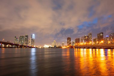 Günbatımında Miami manzarası, ABD. Alacakaranlıkta Miami City gökdelenleri ve deniz üzerindeki yansımalı köprü ile gökyüzü manzarası