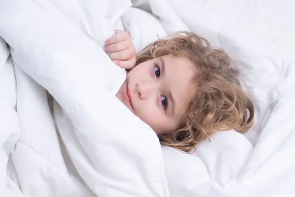 Kid under covers, face cover with blanket. Quietly sleeping. Portrait of little child lying on big bed. Concept of happy children having good time at home. Child awaked up in bed