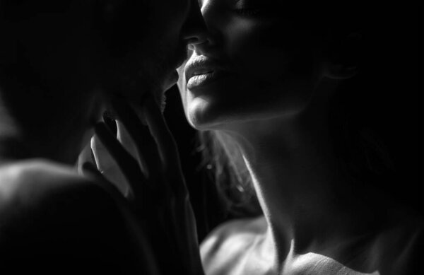 Sensual couple in the tender passion. Close up portrait of woman embracing and going to kiss man. Loving couple kissing over black background. Sexy lips