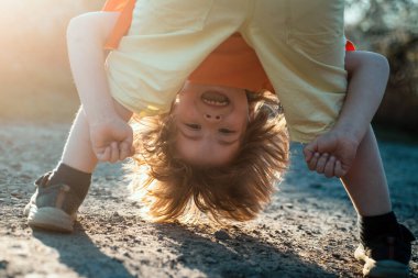Yazın ya da bahar parkında baş aşağı oynayan mutlu çocuk portreleri. Komik çocuk bacağını tut.