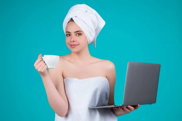 Business woman with towel on head with coffee working on laptop. Morning coffee. Portrait of smiling woman with cup of coffee using laptop, isolated on blue studio background. Freelancer with laptop