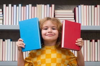 Komik okul çocuğu. Okul kütüphanesindeki masada ödev yapan okul çocuğu. Öğrenci çocuk kitap yığınının yanında ödev edebiyatı okuyor. Çocuk arka planda raflar dolusu kitap olan bir kitap okuyor.