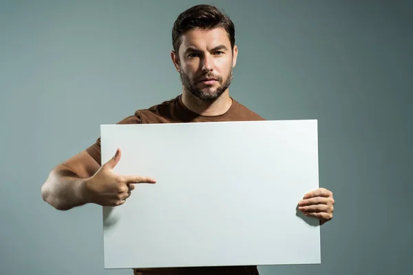 Guy with blank banner ad, isolated on studio background. Man holding empty blank poster showing blank poster pointing finger and gesturing index finger. Male presenting signboard, billboard or banner