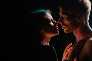 Karanlık arka planda gece lambalarıyla poz veren güzel bir çift. Birbirlerine aşık, kucaklaşan, romantizm ve şefkat dolu genç bir çiftin yüzünü kapatın.