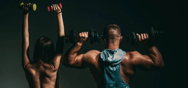 stock image Sexy sport couple exercising with dumbbell. Muscular man with naked body, fitness woman with dumbbells on a dark background, back view. Slim sexy girl with strong muscular man workout