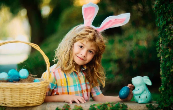 Easter bunny children with rabbit ears in garden hunt egg in easters basket. Child hunting eggs, wear bunny ears hold Easter eggs