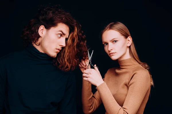 Female with scissors going to do amazing man haircut. Hair salon concept. Hairdresser girl going to cut off long wavy bleached dry hair of customer man. Man hair style, wellness and fashion
