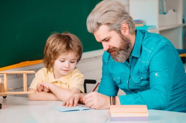 Cute little preschool kid boy with teacher study in a classroom. Young happy family father and son schooling math together. School kids