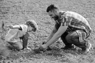 Baba ve oğul toprak zemininde çalışıyorlar. Aile ekimi. Babası küçük çocuğa bahçe işlerini öğretiyor.