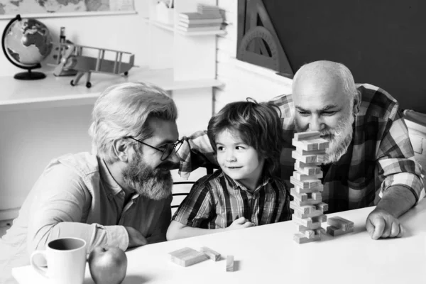 Fathers Day. Elderly man playing his grandson and son. Cute happy boy playing Jenga with his grandfather and father sitting in a class room