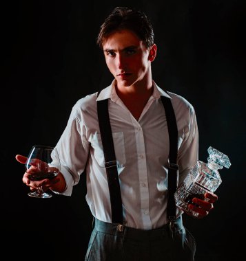 Bardak brendi ya da konyaklı bir adam. Elinde bir bardak viski tutan bir adam. Siyah stüdyoda izole edilmiş viski kadehli bir adamın portresi. Geleneksel viski, beyefendi içkisi.