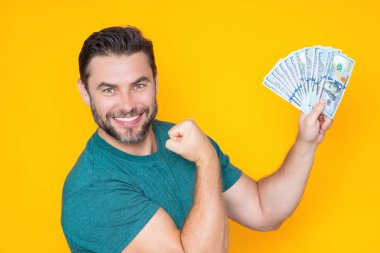 Üzerinde nakit para banknotları olan tişörtlü bir iş adamı sarı stüdyo geçmişinden izole edilmiş. 100 dolarlık banknot, finansal konsept.