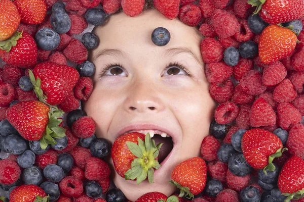 Funny fruits. Berries with kids face close-up. Top view of child face with berri. Berry set near kids face. Cute little boy eats berries. Kid eating vitamins. Close up kids face
