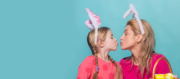 Attractive young woman with little cute girl are preparing for Easter. Mother and daughter wearing bunny ears are kissing. Easter banner, mockup copy space, poster flyer header for website template