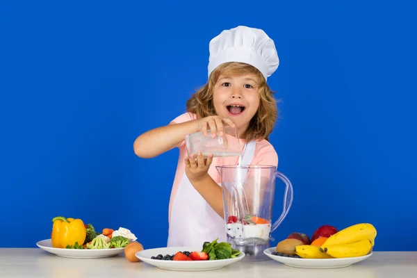 Excited funny chef cook cooking milk shake smoothie. Portrait of chef child in cook hat. Cooking at home, kid boy preparing food from vegetable and fruits. Healthy eating