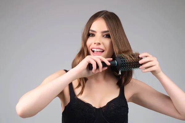Beautiful model girl with comb brushing hair. Beauty woman with straight hair on studio background. Woman holding hairbrush near face. Healthy hair. Hairstyle and hair care concept. Shiny hairs