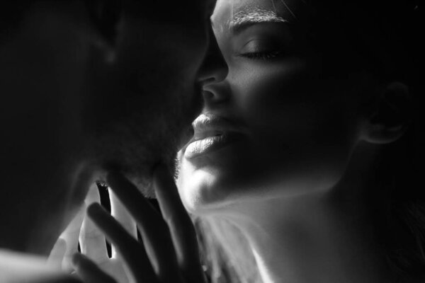 Romantic night date. Close up portrait of man embracing and going to kiss sensual woman. Loving couple kissing over black background. Real love on Valentines Day