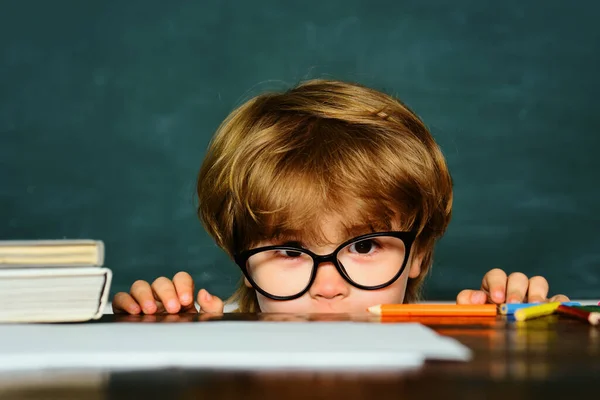可爱的男孩与快乐的脸表达在办公桌与学习用品 孩子在课堂上学习黑板的背景 — 图库照片