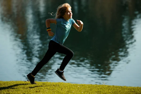 Kids running or jogging near lake on grass in park. Boys runner jogging in outdoor park. Running is a sport that strengthens the body. Kids running on green meadow against sea or lake