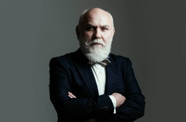 Kolları çapraz yaşlı adam. Gri saçlı, kıdemli, şık takım elbiseli ve kravatlı, kendine güvenen bir iş adamı.