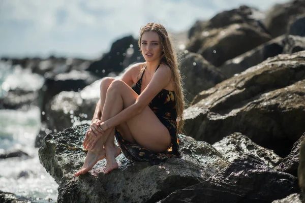 セクシーな女性はビーチの石の岩の上に座っている 美しい砂浜で旅行者の女性の夏のドレス かわいい女の子楽しみます彼女の熱帯の海でリラックスした休日休暇中夏の日 — ストック写真